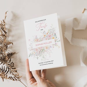 Könnte beinhalten: Eine weiße Karte mit einem floralen Design und dem Text "Willkommen zur Taufe von Sophie Muller" und "Sonntag, 15. November 2027 St. Anna Kirche, Hamburg".
