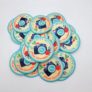 May include: A collection of round, blue and yellow embroidered patches with a camera and the text "Bitty Bitty Photo Committee".