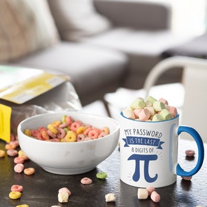 May include: White ceramic mug with a blue rim and handle. The mug has a blue and white graphic that says "My password is the last 8 digits of Pi" with a large blue Pi symbol. The mug is filled with pastel-colored marshmallows and is sitting on a black surface with scattered cereal rings.