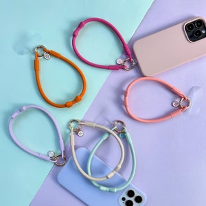 May include: Six colourful silicone phone straps with different coloured rings and charms. The straps are in pink, orange, light blue, and light green. The charms are gold and have letters on them.