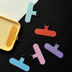 K&ouml;nnte beinhalten: Sechs bunte Fingerh&uuml;te aus Stoff mit einer Schlaufe am Ende. Die Fingerh&uuml;te sind hellblau, rosa, lila, orange und gelb.