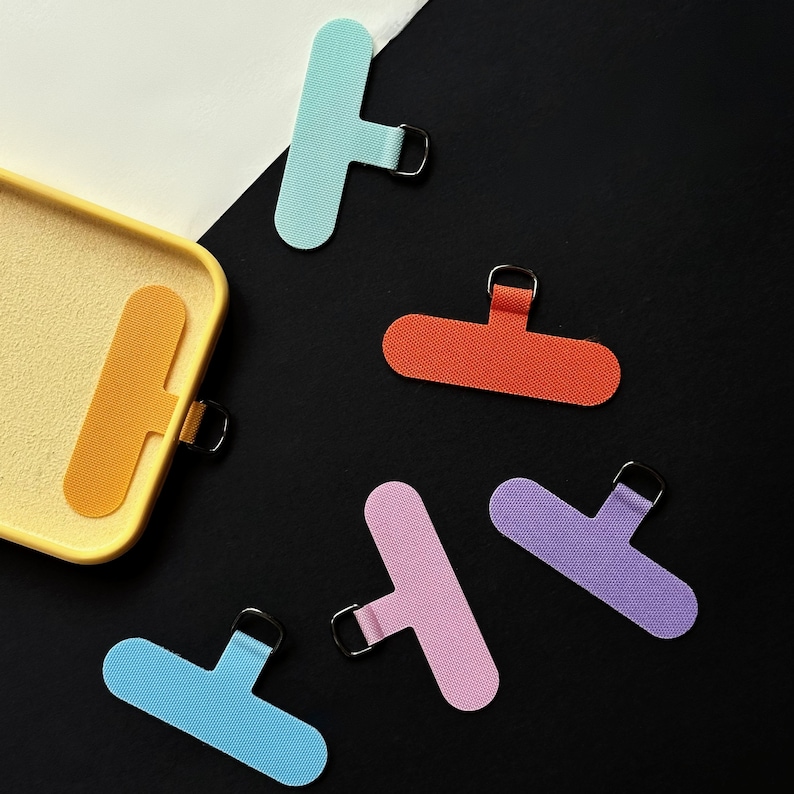 K&ouml;nnte beinhalten: Sechs bunte Fingerh&uuml;te aus Stoff mit einer Schlaufe am Ende. Die Fingerh&uuml;te sind hellblau, rosa, lila, orange und gelb.