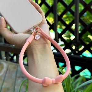 May include: A pink phone strap with a bow and a gold charm with the letter "W" on it.
