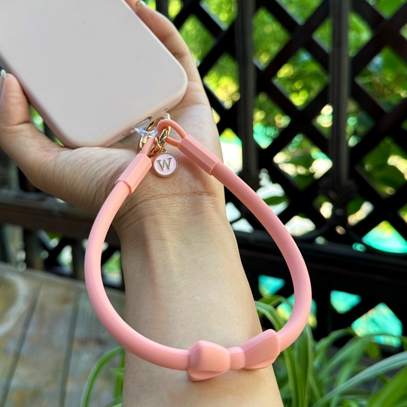 May include: A pink phone strap with a bow and a gold charm with the letter "W" on it.