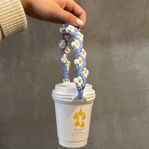 May include: A white to-go cup with a blue and white crocheted handle. The cup has a yellow pear design and the text "ON TODAY" on the front.