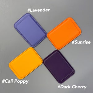 May include: Four different colored leather phone wallets, each with a stitched edge. The colors are lavender, sunrise orange, cali poppy orange, and dark cherry purple. Each wallet has a hashtag with the color name.