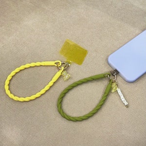 May include: Two phone straps with yellow and green silicone cords and charms. One strap has a yellow bear charm and the other has a green bear charm and a charm with the word "CUSTOM" spelled out in small white letters.