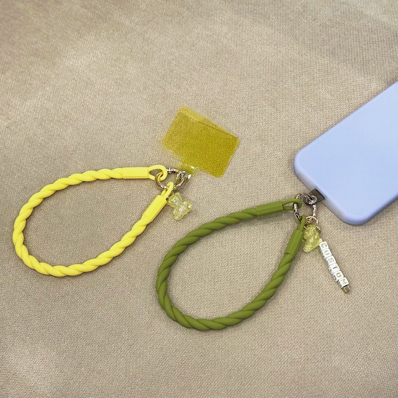 May include: Two phone straps with yellow and green silicone cords and charms. One strap has a yellow bear charm and the other has a green bear charm and a charm with the word "CUSTOM" spelled out in small white letters.