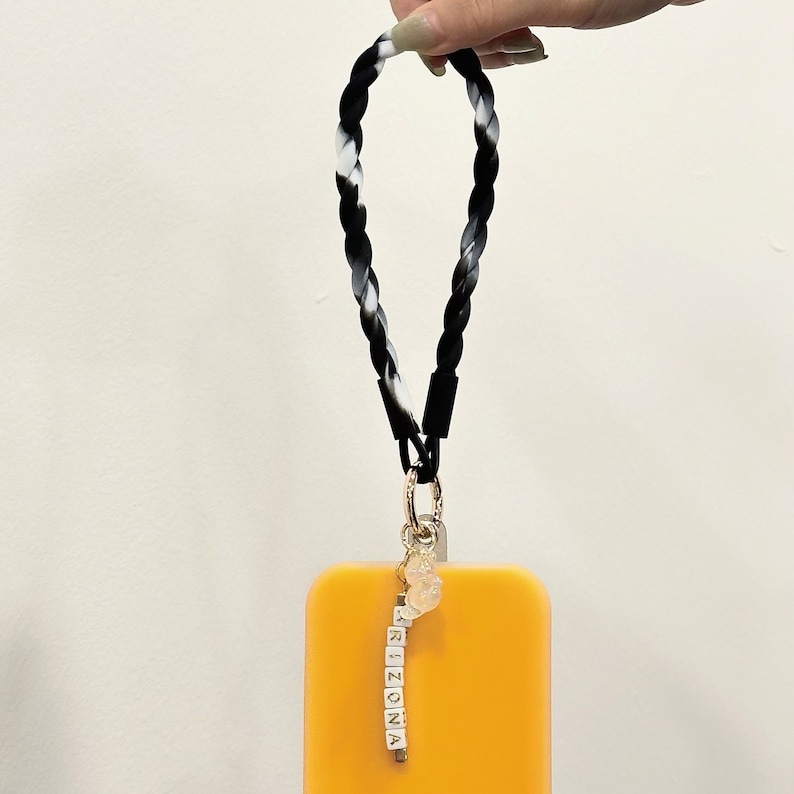 May include: Black and white braided phone strap with a gold charm and a charm with the word "ARIZONA" spelled out in white letters on black blocks.