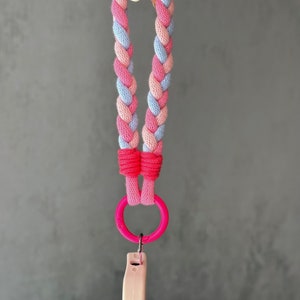 K&ouml;nnte beinhalten: Ein geflochtenes Band in Rosa und Blau mit einem rosafarbenen Kunststoffring und einem rosafarbenen Kunststoffclip.