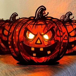 Op de afbeelding: Drie verlichte Halloween pompoen decoraties met uitgesneden gezichten. De pompoenen zijn oranje met zwarte contouren en stelen. Elke pompoen heeft een dreigende grijns en gloeiende ogen, wat een spookachtige sfeer creëert.