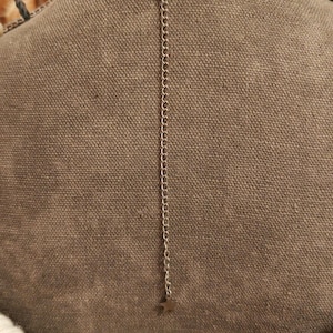 May include: Silver-toned necklace with a delicate chain and a small star pendant. The necklace is displayed on a brown fabric background, showcasing the back of the necklace and its adjustable chain.