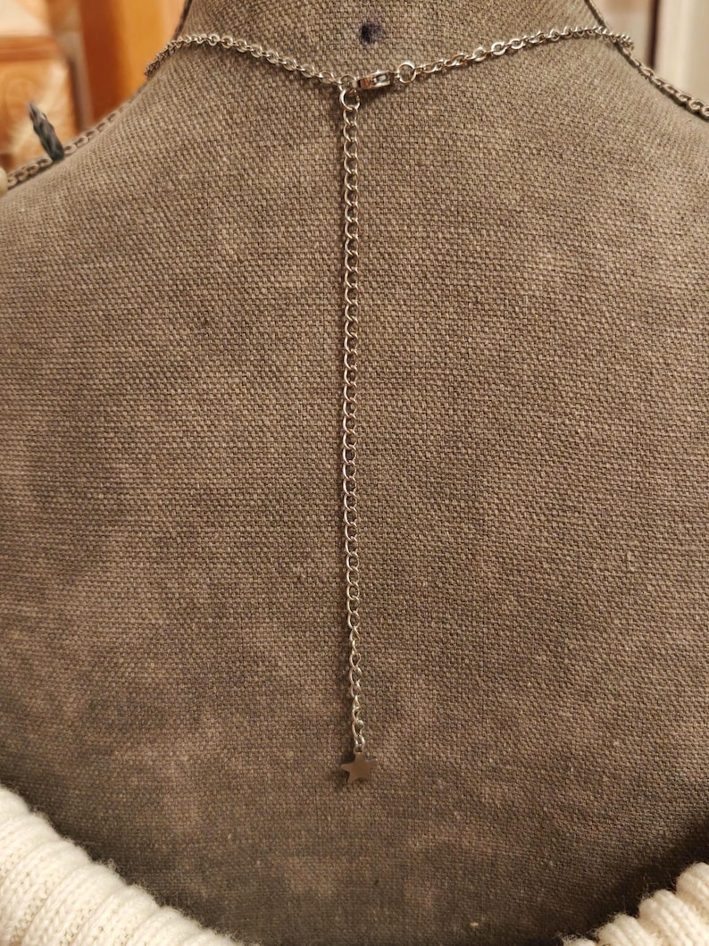 May include: Silver-toned necklace with a delicate chain and a small star pendant. The necklace is displayed on a brown fabric background, showcasing the back of the necklace and its adjustable chain.