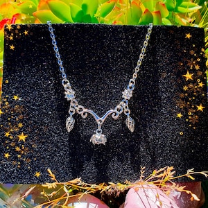 May include: A silver necklace with a delicate pendant featuring a stylised flower and leaves. The necklace has a chain with small crystal accents.