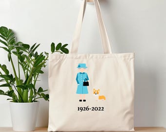 Könnte beinhalten: Eine weiße Canvas-Tragetasche mit einer blauen und weißen Illustration von Queen Elizabeth II und einem Corgi. Der Text "1926-2022" ist unter der Illustration gedruckt.