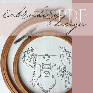 Op de afbeelding: Een borduurring met een babythema-ontwerp. Het ontwerp toont een lijn babykleding, waaronder sokken, een onesie en een konijn, allemaal in een eenvoudige zwarte omtrek. De tekst "Embroidery PDF design" is in cursief geschreven.