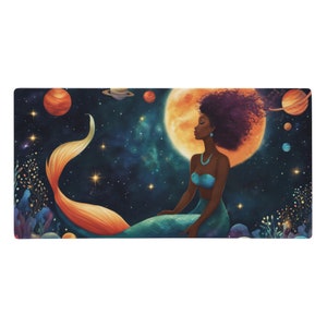 Puede incluir: Alfombrilla de escritorio rectangular con una ilustración de acuarela de una sirena de piel oscura, sentada frente a una gran luna naranja y una galaxia estrellada. La sirena tiene un top y una cola turquesa, con una larga cola naranja y amarilla.