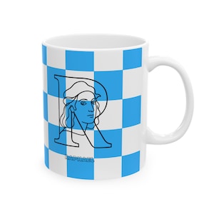 Puede incluir: Una taza de cerámica blanca con un patrón de cuadros azules y blancos. Una ilustración de línea negra de una persona está integrada en una letra R grande, con el texto RAPHAEL impreso en letras mayúsculas negras debajo de la ilustración.