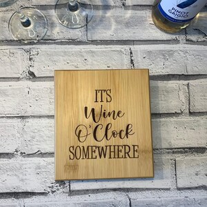 May include: A wooden chopping board with the text "IT'S Wine O'Clock SOMEWHERE" engraved on it. The board is light brown and has a natural wood grain.