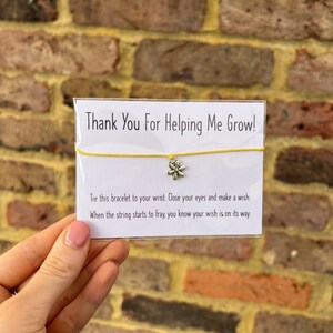 May include: A yellow string bracelet with a silver flower charm. The card reads "Thank You For Helping Me Grow!" and includes instructions to tie the bracelet to your wrist, close your eyes, make a wish, and when the string starts to fray, your wish will come true.