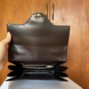 Puede incluir: Bolso de mano de cuero marr&oacute;n oscuro, abierto para mostrar el interior. Cuenta con un cierre dorado y un dise&ntilde;o estructurado con m&uacute;ltiples compartimentos. El interior incluye un bolsillo con cremallera y forro marr&oacute;n oscuro.