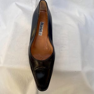 May include: A pair of black leather pumps with a pointed toe. The shoes have a label that reads "Starlet Made in Italy".