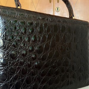Puede incluir: Un bolso vintage marr&oacute;n oscuro con un patr&oacute;n texturizado similar al de un cocodrilo. El bolso tiene un asa superior y una forma rectangular. La superficie tiene un acabado brillante y los herrajes parecen ser dorados.