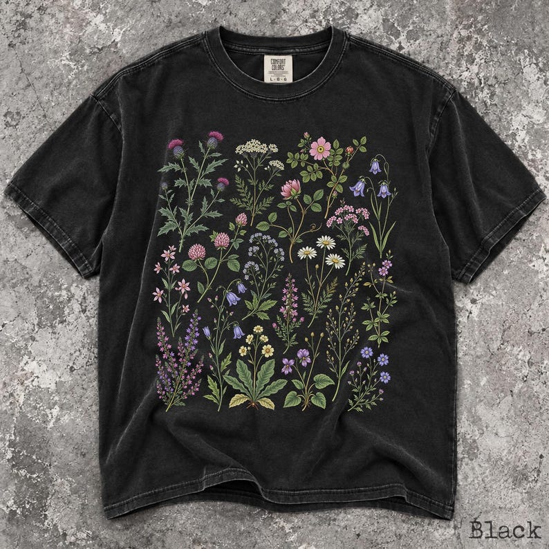 May include: A black short-sleeve t-shirt featuring a botanical print of various wildflowers in shades of pink, purple, yellow, and white. The shirt has a crew neckline and a label at the inner collar that reads Comfort Colors with size L-G-G.