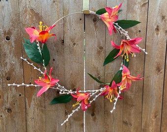 May include: A wreath made of orange and pink flowers with white berries, hanging on a wooden fence.