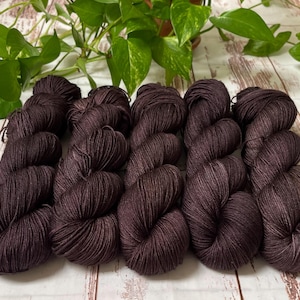 May include: Five skeins of dark brown yarn, arranged in a row on a white wooden surface. The yarn is soft and fluffy, and it has a subtle sheen.