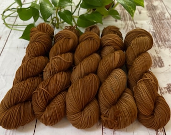 May include: Five skeins of brown yarn, arranged in a row on a white wooden surface.