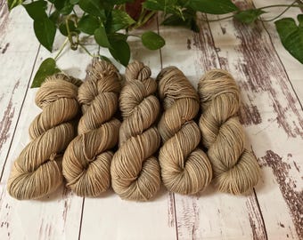 May include: Five skeins of brown yarn, arranged in a row on a white wooden surface.