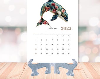 May include: A calendar featuring a watercolor illustration of a dolphin with floral designs. The calendar is for May 2025 and shows the days of the week and dates.