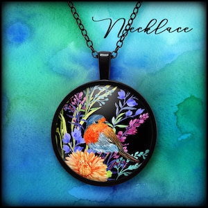 Puede incluir: Collar con colgante negro con una pintura de acuarela de un petirrojo entre flores coloridas. El pájaro tiene pecho rojo, cabeza azul y alas marrones. La cadena y el marco del colgante son negros, con la palabra "Necklace" en cursiva.