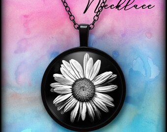 May include: Black daisy pendant necklace with a black chain. The pendant features a black and white image of a daisy flower. The word "Necklace" is written in cursive at the top of the image. The background is a watercolour wash of pink and blue.