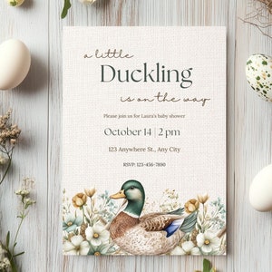 May include: A baby shower invitation with a watercolor illustration of a duckling on a white background with green and white floral accents. The text reads "a little Duckling is on the way". The invitation includes the date, time, and location of the shower.