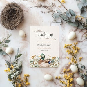 May include: A baby shower invitation with a duckling illustration and floral accents. The invitation reads "a little Duckling is on the way" and includes the date and time of the shower.