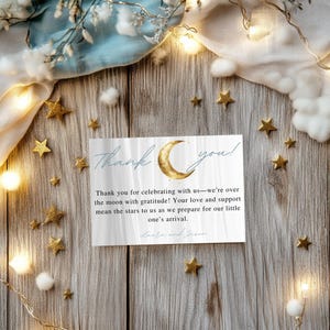 May include: A thank you card with a gold crescent moon and stars on a white background. The text reads "Thank you! Thank you for celebrating with us-we're over the moon with gratitude! Your love and support mean the stars to us as we prepare for our little one's arrival. Laura and Jason"