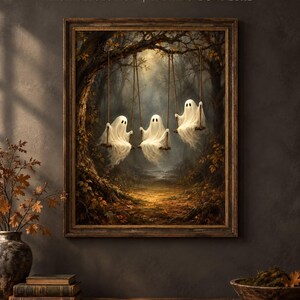 May include: A framed wall art print featuring three white ghosts sitting on wooden swings suspended from a large tree in a dark, autumnal forest. The scene includes fallen leaves on the ground and a soft, glowing light filtering through the trees.