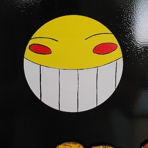 May include: A yellow smiley face with red eyes and a wide, white toothy grin. The smiley face is on a black background.