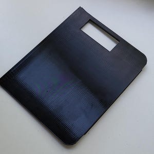 Puede incluir: Una caja rectangular de plástico negro con un recorte rectangular en el centro.