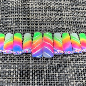 May include: A set of ten colorful fake nails with a tie-dye design and silver glitter accents. Each nail is decorated with iridescent rhinestones.