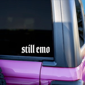 May include: A pink car with a black window and a white vinyl sticker that says "still emo" on the rear window.