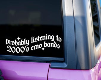 Puede incluir: Una calcomanía de vinilo blanco en la ventana de un coche dice "Probably listening to 2000's emo bands" en una fuente gótica. La calcomanía está en una ventana negra, con la carrocería rosa del coche visible debajo.