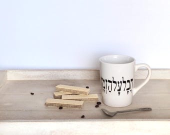 May include: White ceramic mug with black Hebrew text that reads "Hakol LeTova" which means "Everything is for the good" on a white wooden tray with coffee beans and wafer cookies.