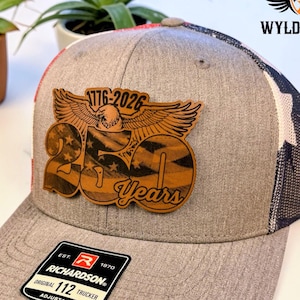 May include: Gray Richardson 112 trucker hat with a leather patch featuring an eagle, American flag design, and the text "250 Years 1776-2026". The hat has a mesh back and adjustable strap.