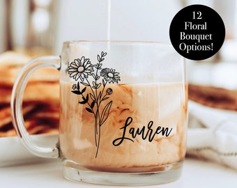 May include: A clear glass mug with a floral design and the name "Lauren" in script. The mug is filled with a light-colored beverage, with cream being poured in. The background includes breakfast items and a coffee maker. Text on the image says "12 Floral Bouquet Options!"