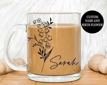 May include: A clear glass mug filled with a light brown liquid, featuring a black floral design and the name "Sarah" in script. The mug is part of a custom design, with the text "CUSTOM NAME AND BIRTH FLOWER!" in a black circle.