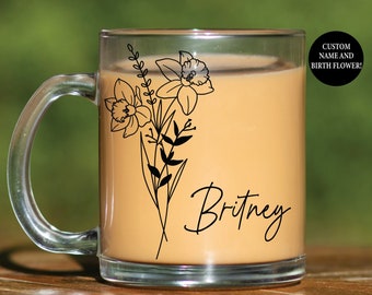 May include: A clear glass mug filled with a light brown liquid. The mug features a black floral design with the name "Britney" in script. A black circle with white text reads "CUSTOM NAME AND BIRTH FLOWER!"