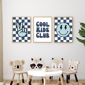 May include: Three blue and white checkered prints with a peace sign, the words "Cool Kids Club", and a smiley face with lightning bolts. The prints are hanging on a white wall above a table with four wooden animal chairs.